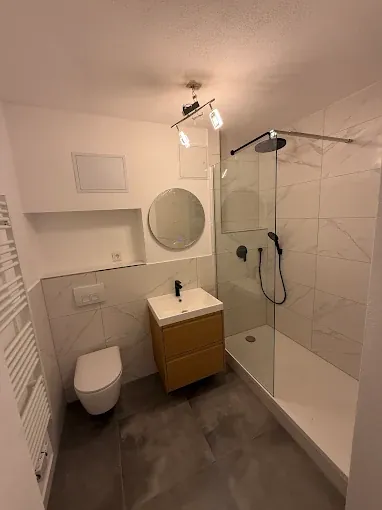 Bad nach der Sanierung: Fliesen in Marmoroptik, begehbare Dusche mit Glaswand, Hänge-WC und Waschtisch mit Holzfront